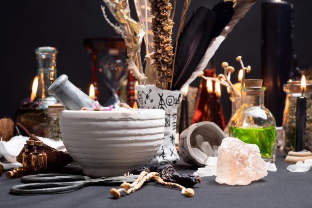 na stole je položena bílá keramická miska, kolem jsou různé léčivé bylinky, svíčka a odvary.